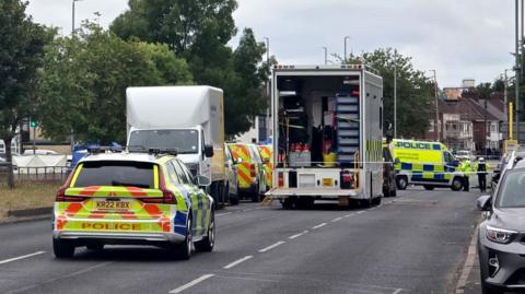 A number of police vehicles close off dual carriageway in Merseyside. The road has trees lined down the middle