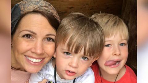 Natalie Hull, wearing a pink top and smiling with her two sons one wearing a red t-shirt and the other wearing white.