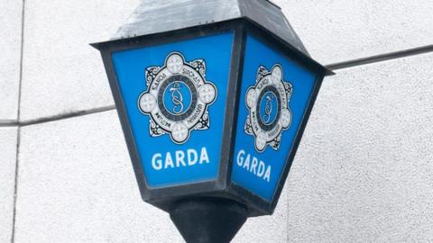 A Garda sign with a blue background. It reads 'GARDA' in white with the forces emblem. 