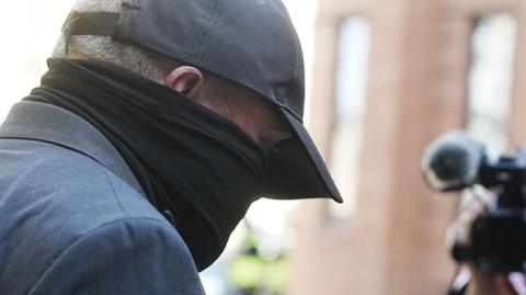 Robert Bush arrives at Hull Crown Court, he is wearing a dark suit and a baseball cap and has heavy scarf obscuring his face