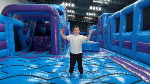 Ted standing on an inflatable obstacle course with his arms in the air.