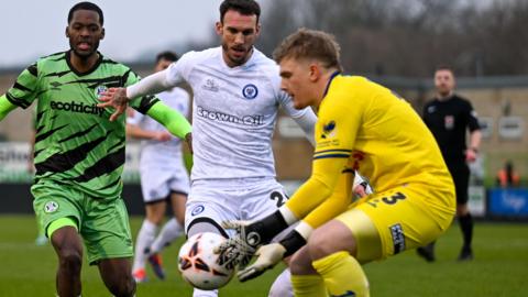 Sam Waller, in yellow, comes out of his goal to gather the ball under pressure from a Forest Green Rovers player during a match