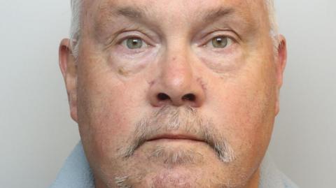 Headshot of an older man with short white hair and a grey thinning moustache and goatee beard.