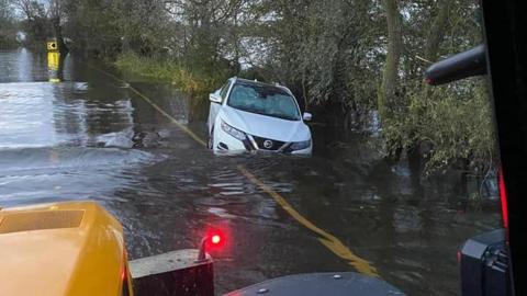 A white Nissan stuck in flood water on the edge of the road.