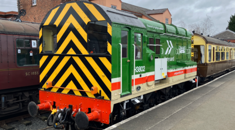A locomotive is painted yellow and black at the front and mainly green down the side. The photo is taken from the platform and the side includes the words Vanguard, Severn Valley Railway and powered by hydrogen.
