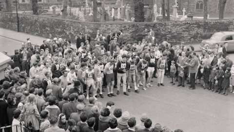 A black and white photograph of a group of people gathered around the starters of the Parish Walk. In the background is a church graveyard.