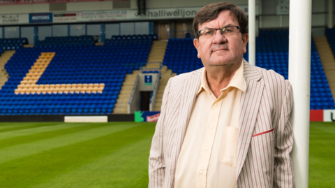 Professor Steven Broomhead, the outgoing chief executive of Warrington Borough Council, stands against the goalposts at Warrington Wolves' rugby league stadium.