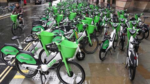 Rows of bright green Lime rental e‑bikes on a wide pavement seen extending in to the distance