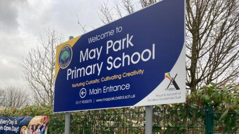 The sign at the front of May Park primary school bearing its name and logo which is a tree in a circular badge