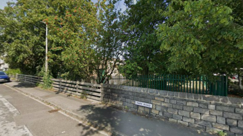A road with a pavement running down the side and a road sign which says 'Park Road'. 