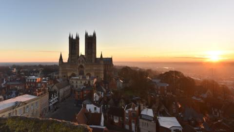 Lincoln Cathedral surrounded by buildings with a sunset sky behind it.