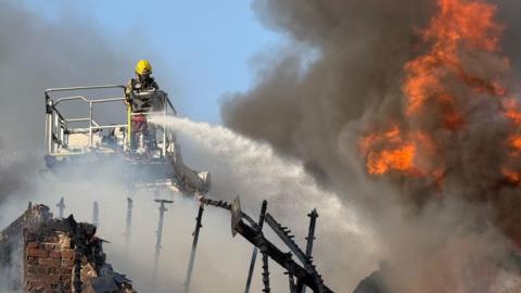 A firefighter on a crane shooting water jets down towards a building