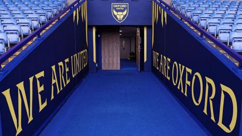 The Oxford United tunnel, viewed from pitchside, with a blue carpet leading to one door open