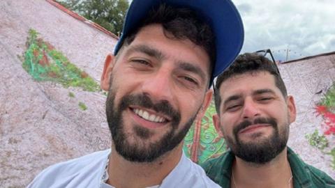 Twin brothers Gali and Ziv Berman smile in a close-up photo. They both have beards and are wearing white and green shirts.