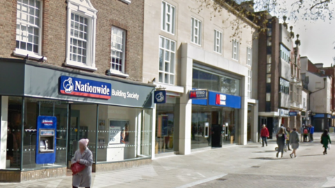 The outside of Nationwide building society, with a shopper walking past, taken in 2019.