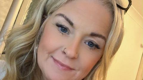 Melanie Stinton takes a selfie. She has curly blonde hair and is wearing her glasses on her head.