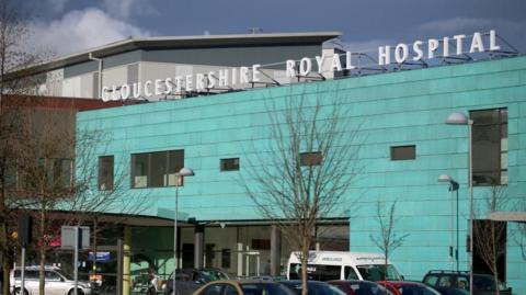 The front of Gloucestershire Royal Hospital which is turquoise blue and has the name of the hospital in big white letters on the roof