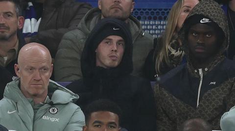 Cole Palmer watching Chelsea's match from the stands while dressed in a hoody