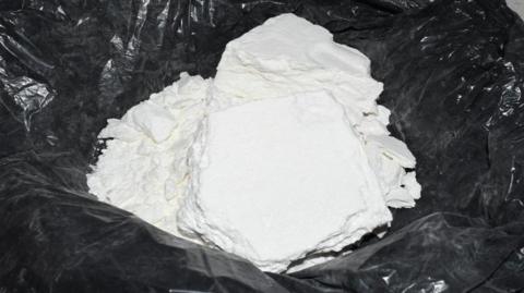 A large pile of soft white powder lies in the middle of a black plastic bag