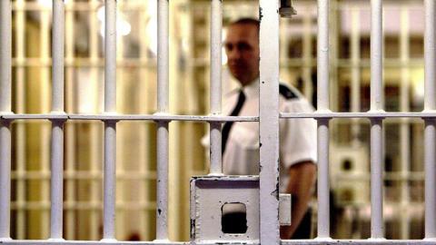 A prison guard at HMP Pentonville stands behind a locked gate 