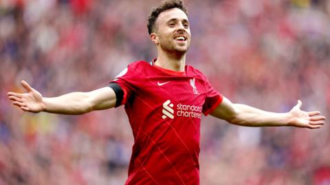 Diogo Jota celebrates scoring a goal with his arms outstetched playing for Liverpool in their red home kit in 2021.