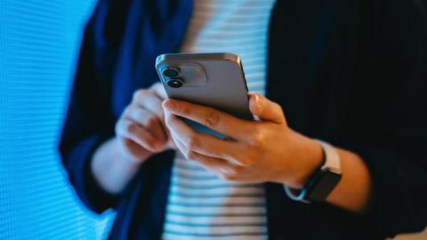 A young woman holds a smartphone in her hands. 