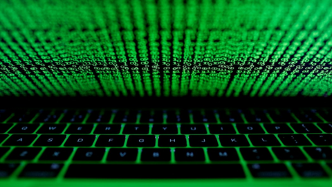 A computer keyboard with black keys illuminated in green. There are random digits in green scrolling down the screen