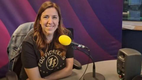 Lisa Peacock sitting behind the desk in the 鶹ҳ Radio Tees studio. A yellow microphone has been placed in front of her.