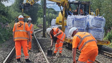 Men in orange work gear use shovels to put down hardcore on a section of the tramway between Oldham and Rochdale. 