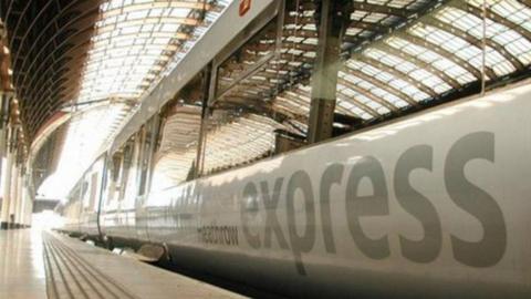 A stationary train with a sign saying Heathrow express on its side. Light is coming through the end of the track.