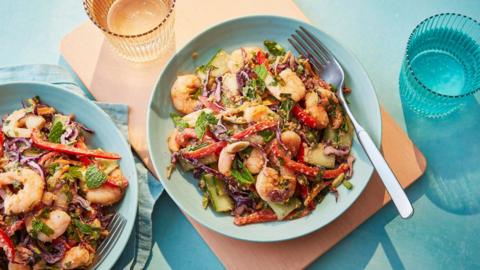 A salad with prawns, red pepper, cucumber and carrot on a blue plate with a fork