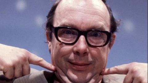 Eric Morecambe with each hand pointing to his mouth