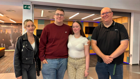 Two men and two women stand in a line and smile at the camera.