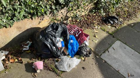 Black bin split open on the street with rubbish coming out of it