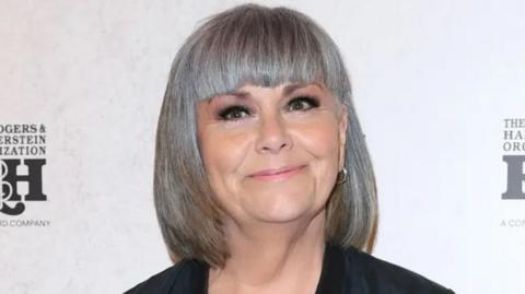 Dawn French wears a black coat at a function and is looking at the camera.