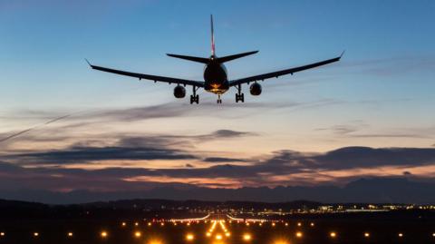 A plane about to land on a runway as the sun sets