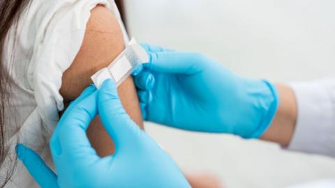 Doctor applies bandage to preteen girl's arm following an immunization.