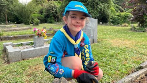 Girl in blue jumper crouched down next to a grave