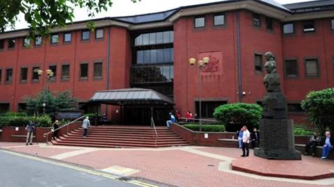 The exterior of a large red brick building with dark windows and steps leading up to a large entrance