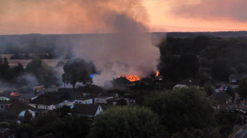 Orange flames consume the roofs of two properties with smoke trailing into the sky in an aerial shot.