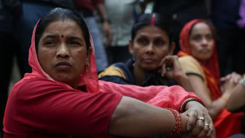 Three women factory worker - wearing saree - sit, as they participate in a protest demanding wage hikes from their company, in Haryana's Manesar on 7 April 2026. 