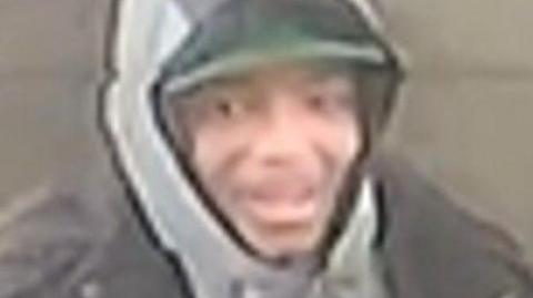 A grainy CCTV still of a young man in a grey hoodie.