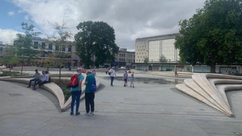 People passing through Kings Square in Gloucester, with the former Debenhams building in the background