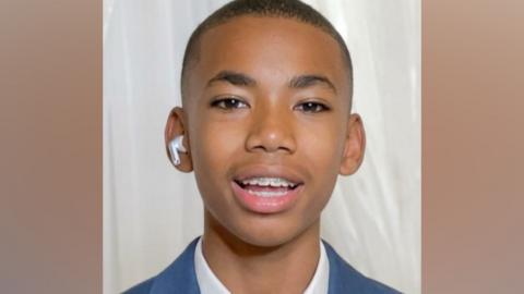 Head shot of Jamal Coombes who is wearing a white shirt beneath a blue jacket. He has a white air pod in one ear