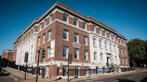 A red brick building in the sunshine. The sky is blue. 