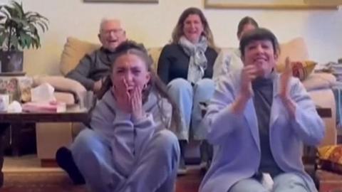 Family member cheer and clap while sat in living room seeing hostages released