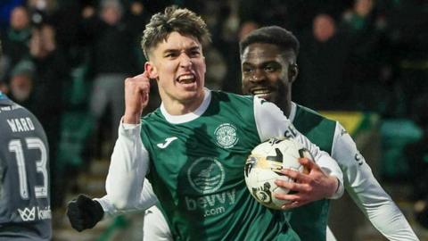 Hibs striker Kieron Bowie celebrates as he clenches his right fist and carries the ball in his left hand