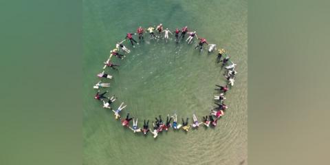 An overhead shot of a large group of people in a circle in the sea