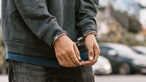 Under arrest, a man's hands with clenched fists are handcuffed behind him.