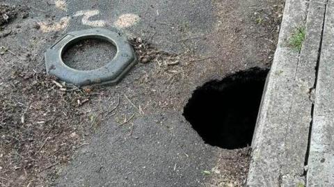 A road in Castle Cary, Somerset, with a hole on the side of the road right next to the pavement.
